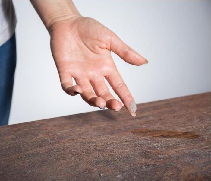 person showing a dusty table with dust on their fingertip